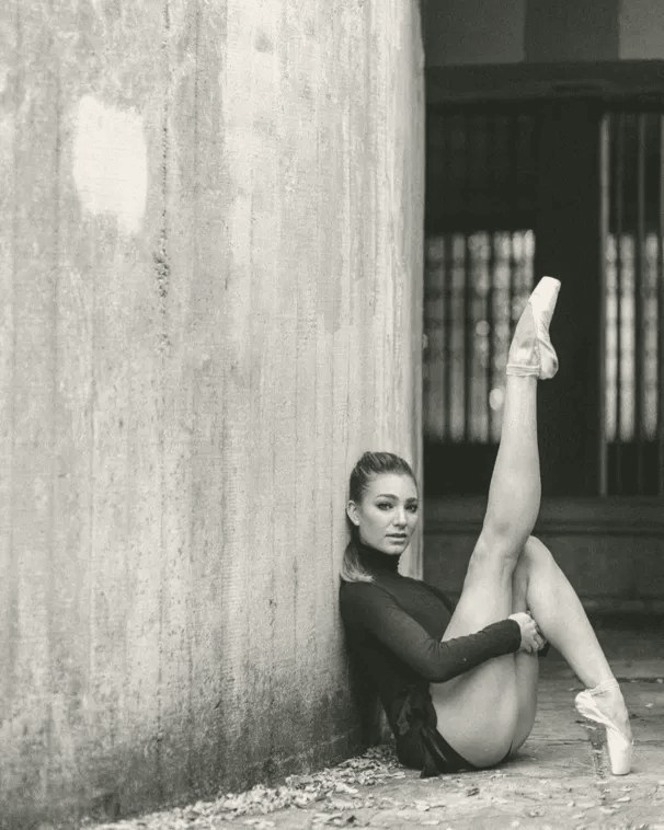 Alexandra Grace, leg extended in a ballet line against a concrete wall